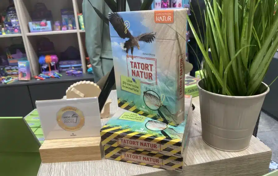 Die Verpackung des Kartenset-buches "Tatort Natur" steht auf einem Tisch, rechts davon die Auszeichnung für das Jugend Sachbuch 2025